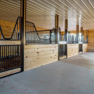 Wooden horse stalls with protective grill windows and a white entry door. Custom finish options available.