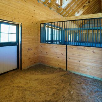Horse stable interior with Dutch door and protective stall grills, featuring natural wood finish and ample ventilation.