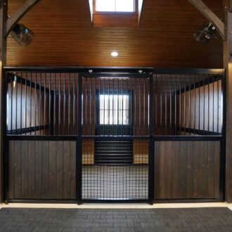 Wooden stall with protective mesh and dark finish, featuring sliding barn and entry doors in a well-lit interior.