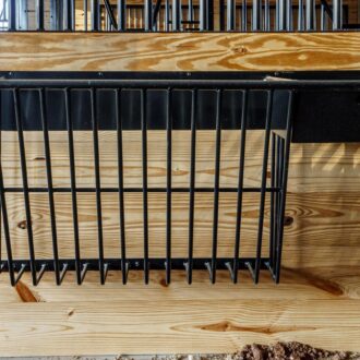 Black protective stall grill on wooden wall, ideal for sliding barn doors and carriage doors. Custom finish options available.
