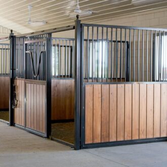 Wooden horse stalls with black protective grills and mesh, featuring sliding barn doors and custom finish options.