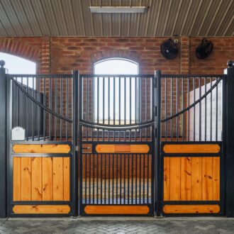 Elegant horse stall with protective black grills, wooden panels, and brick walls in a barn; features a sliding stall door.