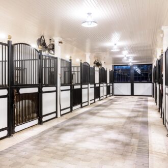 Modern stable interior with protective stall grills and customizable finishes, featuring sliding barn-style doors.