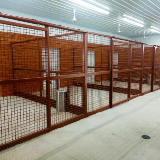 Horse stalls with brown protective mesh panels, sliding stall fronts, and fans, offering custom finish and color options.