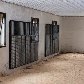 Horse stable interior with protective stall grills, mesh panels, and prop-out windows for ventilation and safety.