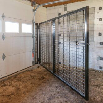 Stall with sliding metal door featuring protective grill, adjacent to a sectioned garage door.