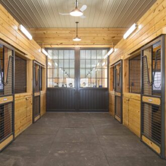 Wooden barn interior featuring sliding stall doors with protective mesh and loft doors, showcasing natural finish options.
