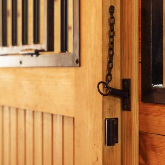 Wooden dutch door with black protective stall grill, chain latch, and natural finish. Ideal for barn entry.
