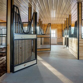 Spacious stable with wooden sliding barn doors and protective stall grills, showcasing natural finish and bright interior.