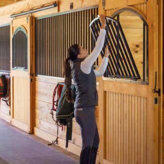 A woman opening a horse stall window