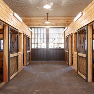 Barn interior with sliding stall doors, featuring protective stall grills in natural wood finish.