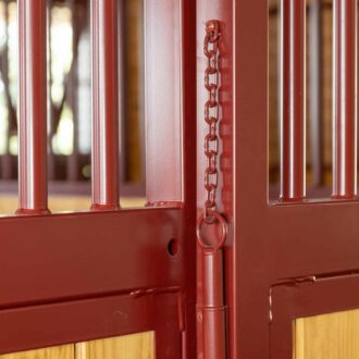Red metal stall door with protective stall grills and wood panels, featuring a sturdy chain latch.