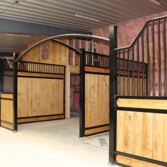 Wooden horse stalls featuring sliding doors with black metal frames and protective grills, ideal for stables.