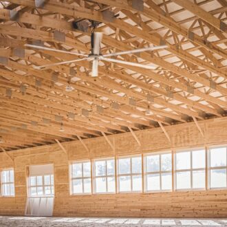 Spacious equestrian arena interior with natural light through numerous arena windows, showcasing finished wood beams.