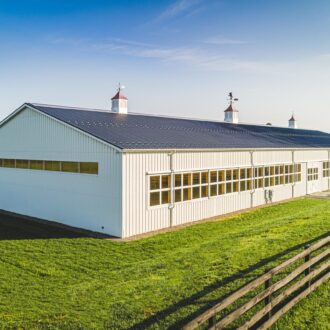 White barn with sliding doors and large arena windows.