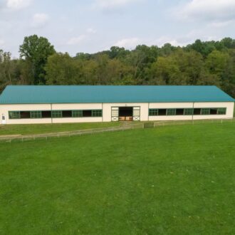 Large barn with green sliding doors and arena windows, showcasing durable build and classic finish.