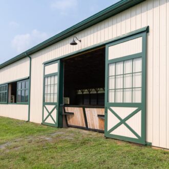 Large barn with green sliding doors and arena windows, showcasing durable build and classic finish.