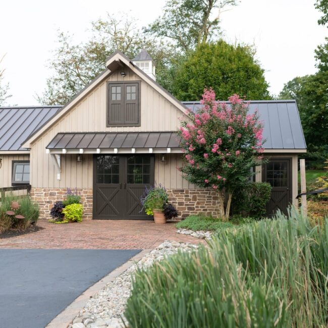 Barn with sliding loft doors, entry doors, and dutch windows. Features include stone finish and garden landscape.