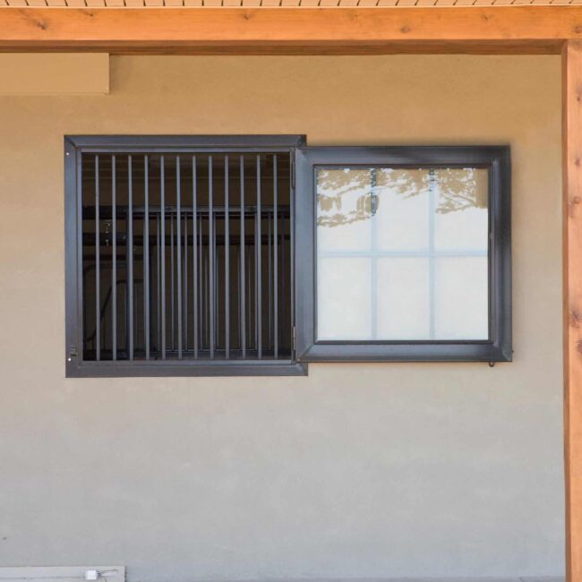 Dutch window with protective grills and black finish, under a wooden structure, ideal for barn or loft installations.