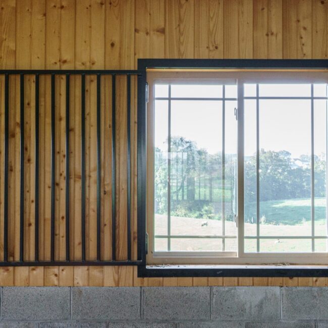 Sliding barn window with protective grill, showcasing wooden frame, natural finish, and exterior view through glass panels.