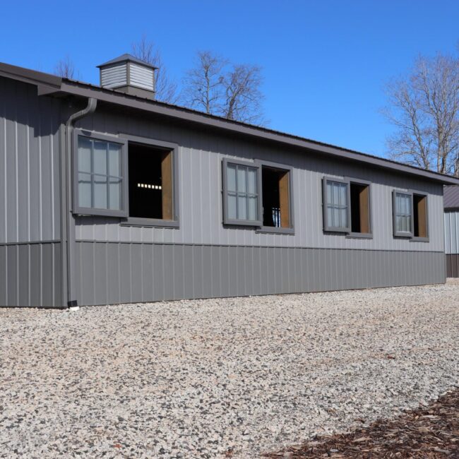 Gray building with open awning windows, protective stall grills, and gray finish. Clear sky and gravel foreground.