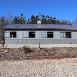Gray barn featuring sliding loft doors and awning windows, nestled in a rustic landscape. Ideal for custom finish options.