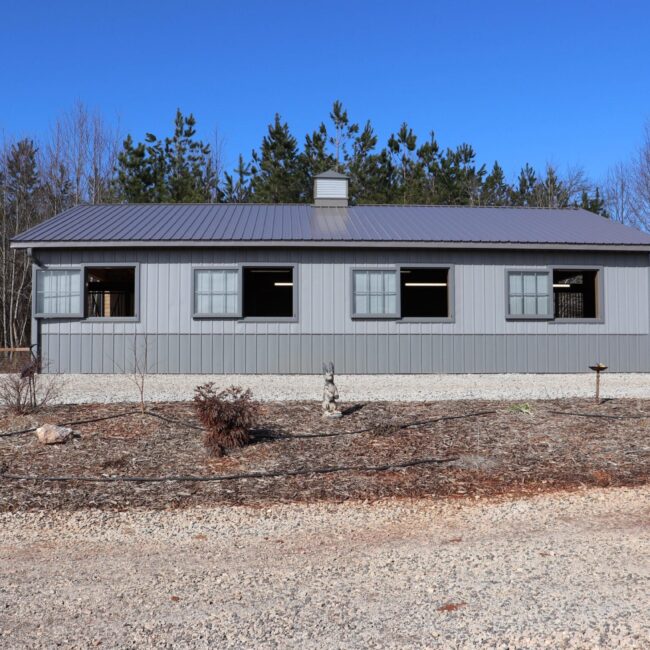 Gray barn featuring sliding loft doors and awning windows, nestled in a rustic landscape. Ideal for custom finish options.