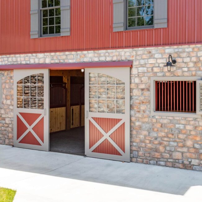 Red sliding barn doors and Dutch windows with mesh grills on a rustic stone barn exterior.