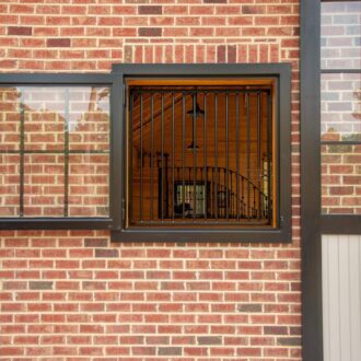Dutch window with protective stall grills on a brick wall; black metal frame, prop-out design for ventilation.