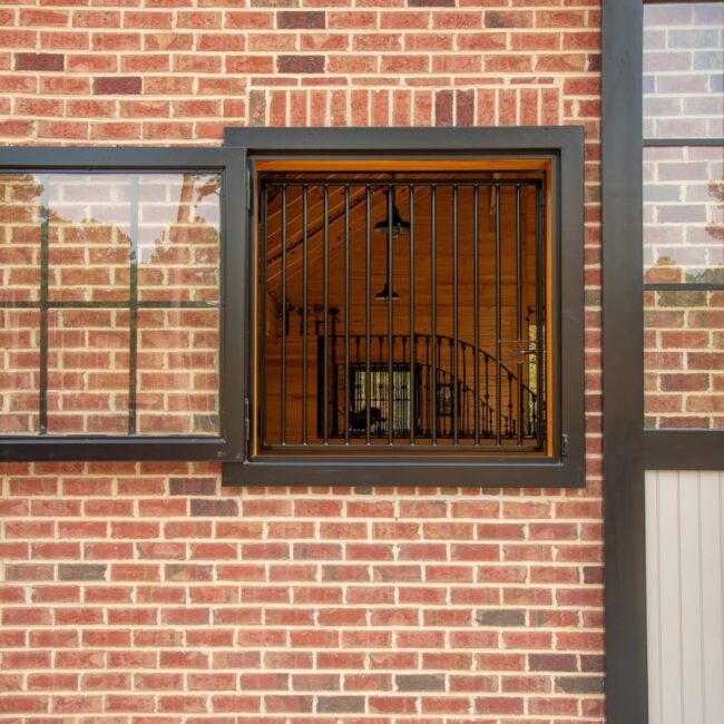 Dutch window with protective stall grills on a brick wall; black metal frame, prop-out design for ventilation.