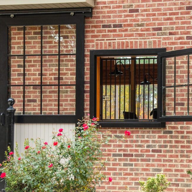 Open Dutch window with black frame on brick wall, highlighting stylish entry doors and stalls with protective grills.