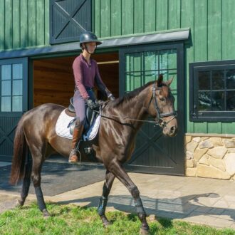 Rider on horse near green barn with sliding barn doors, dutch windows, and stone base.