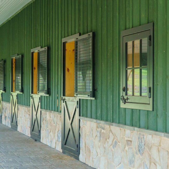 Green barn with stone walls featuring mesh Dutch windows, each paired with X-brace Dutch doors for optimal ventilation.