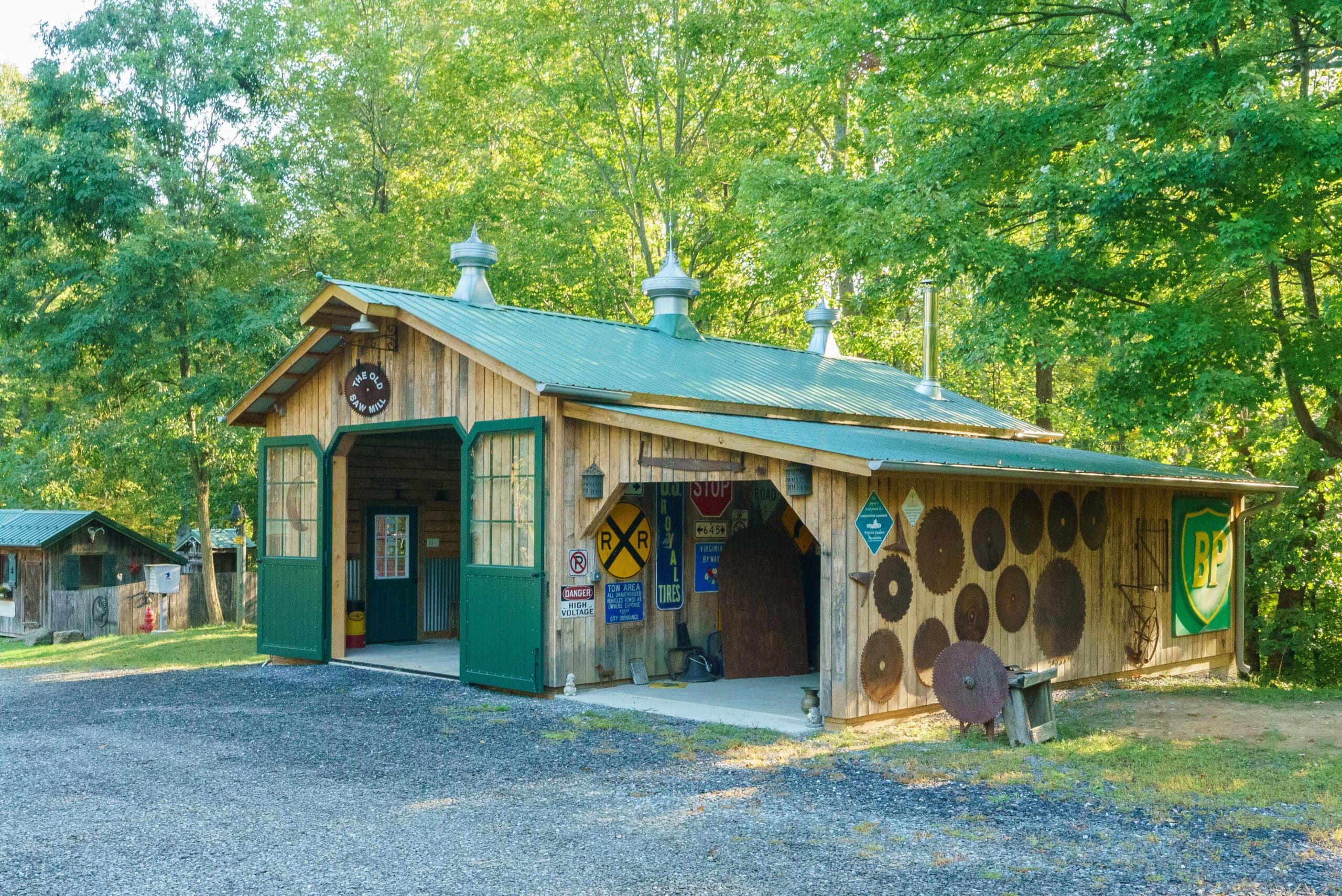 Rustic barn with green carriage doors, featuring vintage signage and a metal roof. Surrounded by lush trees.