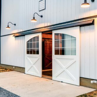 White sliding barn doors with glass windows open on a barn, highlighting entry doors and custom finish options.