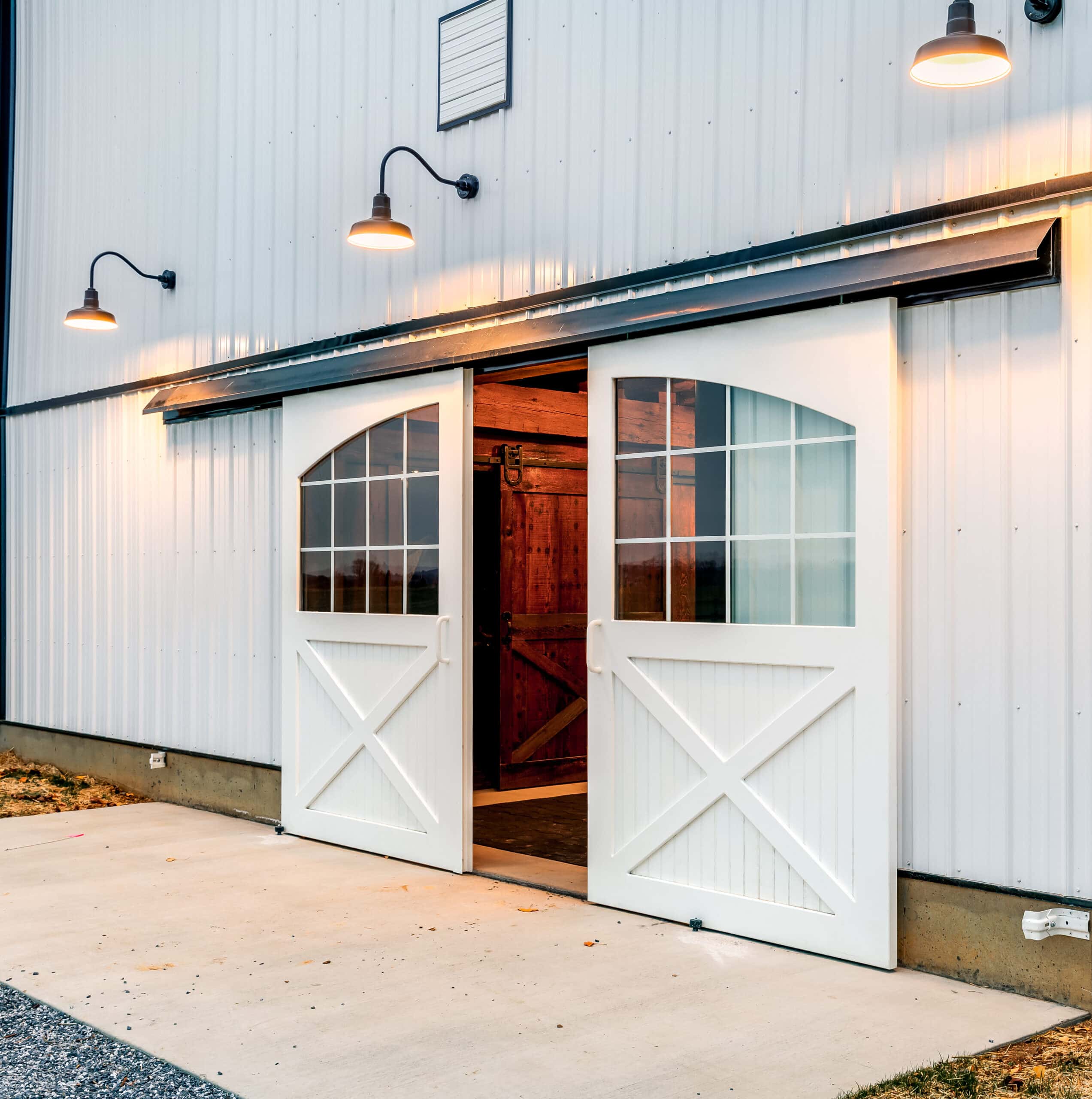 White sliding barn doors with glass windows open on a barn, highlighting entry doors and custom finish options.