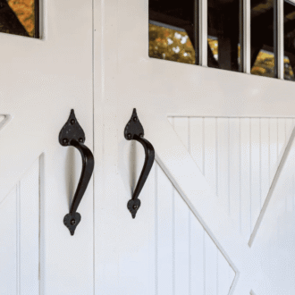 White carriage doors with black handles, featuring glass panels, in a fall setting. Perfect for custom entry solutions.
