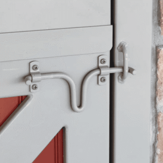Close-up of a sliding barn door latch with red paneling, featuring rustic finish and stone wall backdrop.