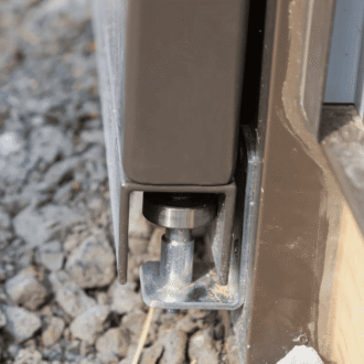 Close-up of sliding barn door bottom track on gravel, showcasing durability and smooth sliding mechanism.