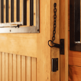 Pin latch on wood stall door with black protective grill.