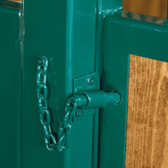 Green metal protective stall grill on a wooden sliding barn door with pin latch, showcasing hardware finish options.
