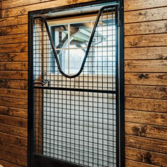 Barn door with protective mesh grill, medium wood finish, featuring a dutch window for ventilation and style.