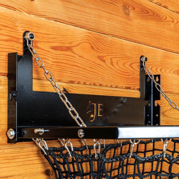 Black mesh haynet hay feeder on wooden wall with chain suspension. Ideal for barn use.