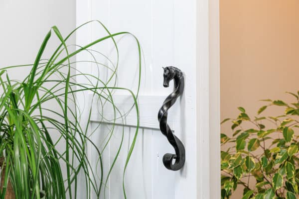 Black finish horse-head shaped handle, surrounded by greenery. Highlights custom design, rustic appeal.