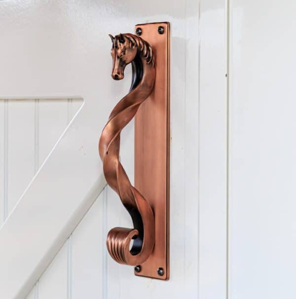 White sliding barn door with decorative copper handle featuring a horse head design, showcasing elegant finish options.