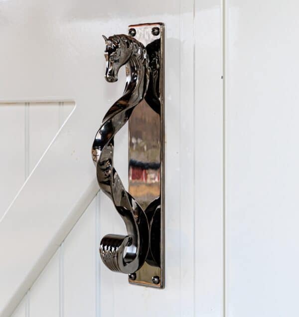 Ornate horse-head handle on a white sliding barn door, featuring a glossy, metal finish for classic elegance.