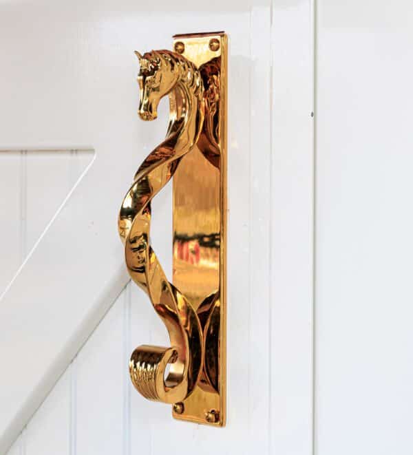 Gold horse head handle on white sliding barn door, showcasing elegant finish options for entry and carriage doors.