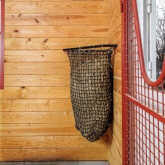 EZ-fill haynet with protective stall grills and mesh, installed in a wood-paneled barn.