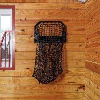 Black EZ-fill haynet hanging on wooden stall wall with protective mesh window and red trim.
