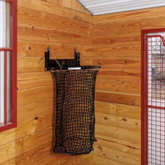 Black EZ-fill haynet on wooden stable wall, red mesh stall grill, white Dutch window with protective red stall bars.